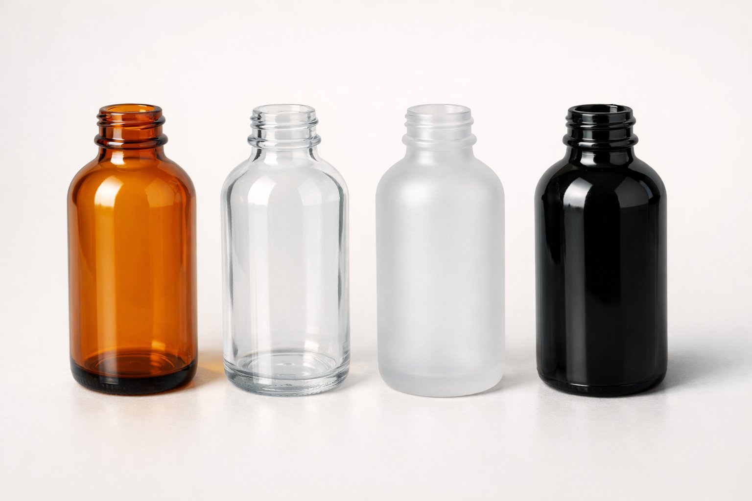 Four glass bottles in a row showing amber, clear, frosted, and black glass colors on a neutral background.