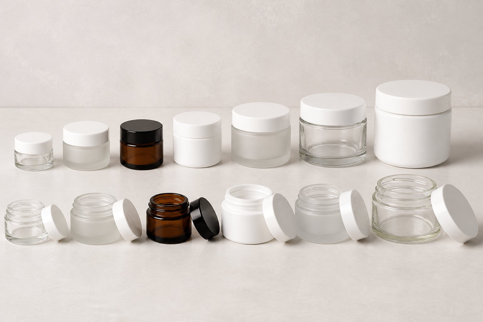 An assortment of empty cream jars in different materials and sizes arranged from smallest to largest on a neutral studio surface.